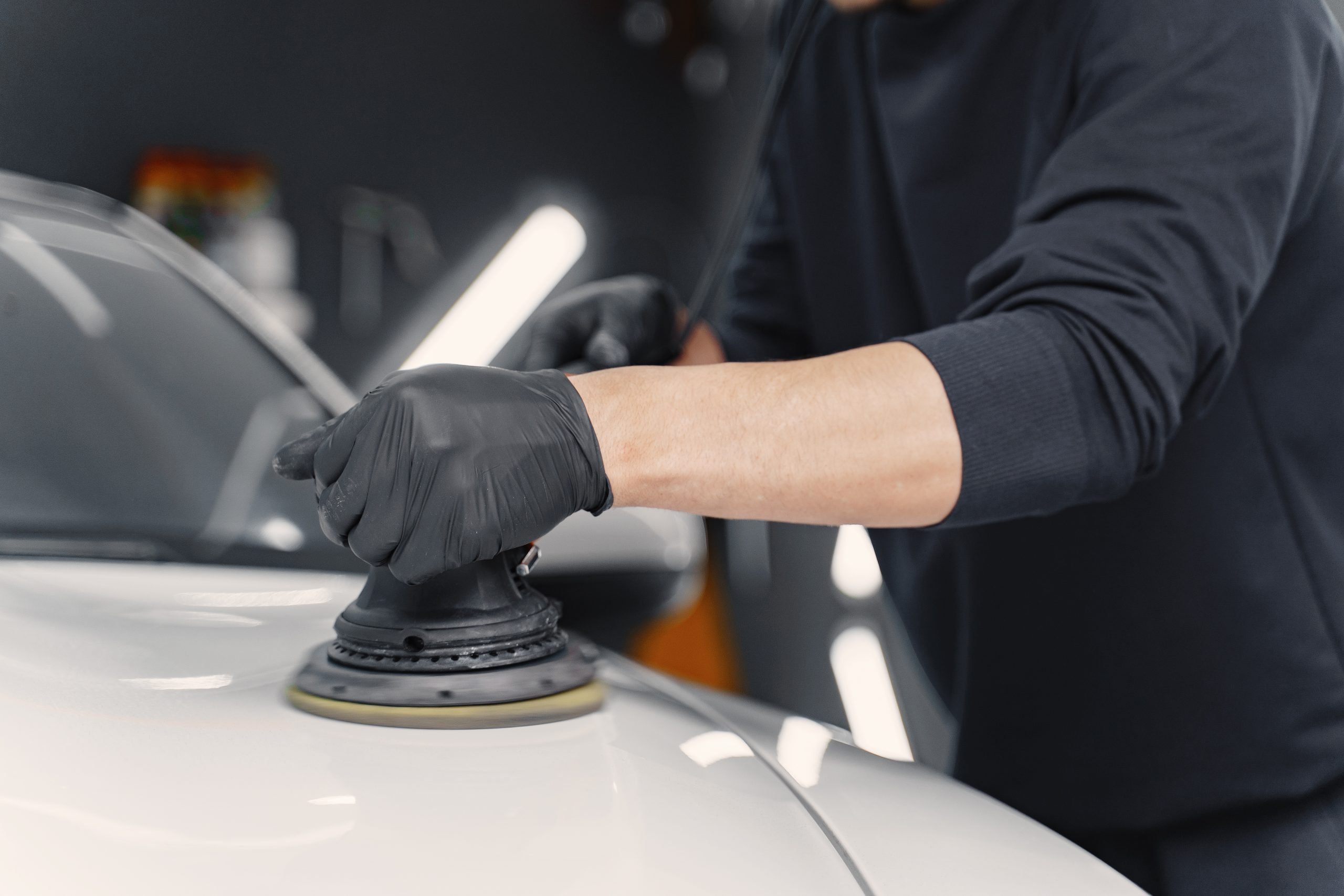 Man in a garage. Worker polish a car. Man in a black uniform.